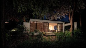Uma casa moderna com uma grande porta de vidro, rodeada por vegetação densa.
