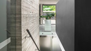 Um corredor estreito com uma porta de vidro que dá para uma varanda, corrimão de metal e um vaso de planta sobre uma mesa de vidro.