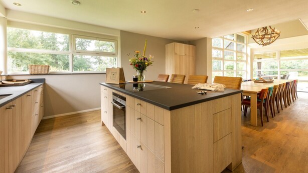 A modern kitchen with a large island, wooden cabinets, and a dining area with a long table and chairs. - Achterhoek Villa with Heated Pool (Aalten)