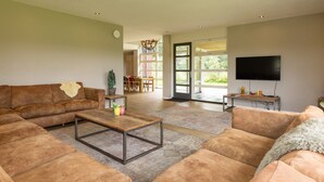 A spacious living room with a large sofa, a coffee table, and a television. - Achterhoek Villa with Heated Pool (Aalten)