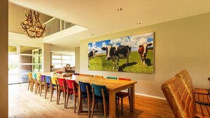 A dining area with a long wooden table, colorful chairs, and a large painting of cows on the wall. - Achterhoek Villa with Heated Pool (Aalten)