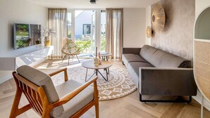 A modern living room with a sofa, chairs, a coffee table, and a large window with curtains. - Holiday Home Near North Sea for 6 (Sint Maarten)