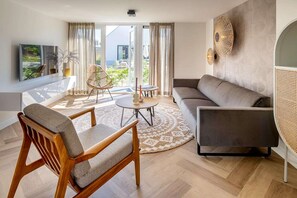 A modern living room with a sofa, chairs, a coffee table, and a large window with curtains. - Holiday Home Near North Sea for 6 (Sint Maarten)