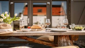 A dining table set with food and drinks, a vase of flowers, and a bottle of water. - Holiday Home Near North Sea for 6 (Sint Maarten)