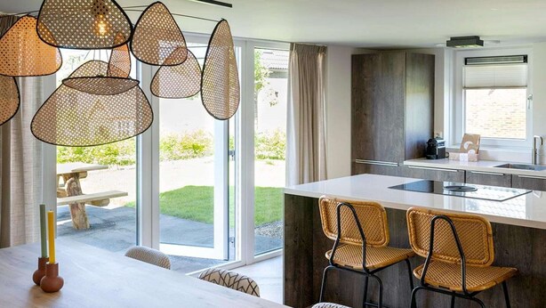 A modern kitchen with a large island, wicker chairs, and a dining table with candles. - Holiday Home Near North Sea for 6 (Sint Maarten)