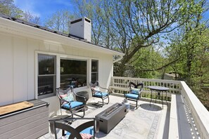 Een terras met buitenmeubilair, een vuurplaats en uitzicht op bomen.