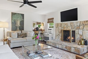 Una sala de estar con chimenea de piedra, un sofá, una mesa de centro con libros y un televisor montado en la pared.