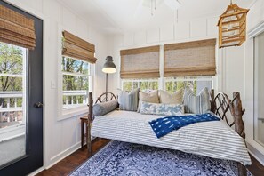 Een slaapkamer met een bed, kussens, een lamp, een houten hoofdbord en een raam met jaloezieën.