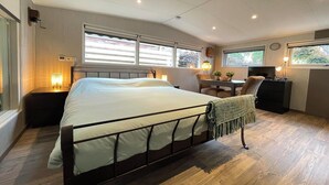 Ein Schlafzimmer mit Bett, Nachttisch, Lampe, Fernseher, Schreibtisch, Stuhl und Fenstern.