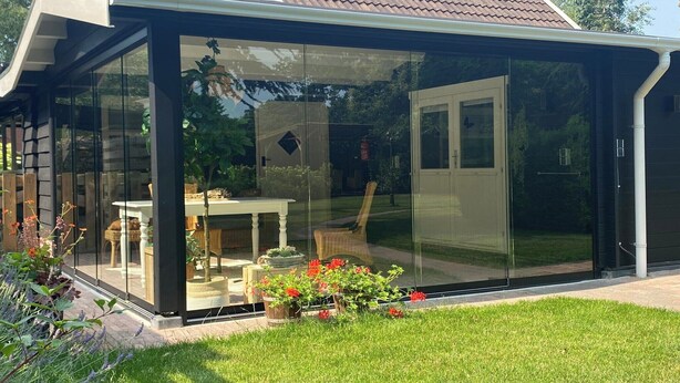 Ein modernes Haus mit einer gläsernen Veranda, einer Tür und einem sichtbaren Gartenbereich.