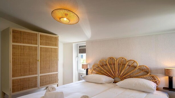 A hotel room with a large bed, a wicker headboard, a wardrobe, and a ceiling light fixture. - Modern Dune Retreat with Garden (Sint Maarten)
