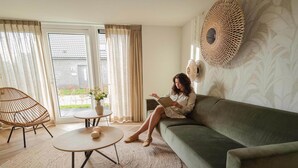 A living room with a sofa, a round coffee table, a wicker chair, and a view through a glass door. - Modern Dune Retreat with Garden (Sint Maarten)