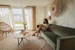 A living room with a sofa, a round coffee table, a wicker chair, and a view through a glass door. - Modern Dune Retreat with Garden (Sint Maarten)