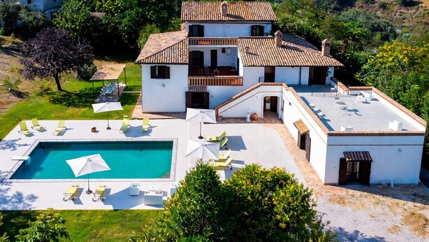 A two-story house with a swimming pool, outdoor seating, and a view of the surrounding landscape.