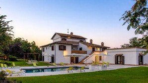 A two-story house with a swimming pool, outdoor seating, and a well-maintained lawn.