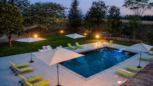 A swimming pool with lounge chairs and umbrellas, surrounded by a grassy area and trees.