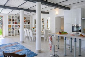 A modern kitchen with white cabinets, a dining area with white chairs, and a bookshelf filled with books. - Villa Denise Winter Villa with Private Pool Near Rome (Abruzzo)