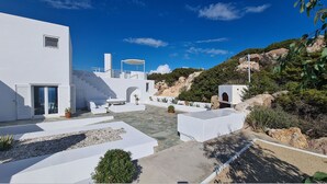 Un edificio moderno blanco con un patio, zona de estar exterior y una escalera que conduce a una terraza.