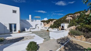 A modern white building with a patio area, outdoor seating, and a staircase leading to a terrace. - Sunset villa-Infinity pool-spa- Boule (Paros)
