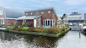 Een gebouw aan de rivier met een overdekt terras, een steiger met boten en een kanaal.