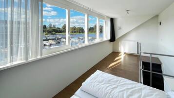 A room with a large window overlooking a marina, a bed with white bedding, a radiator, and a metal staircase.