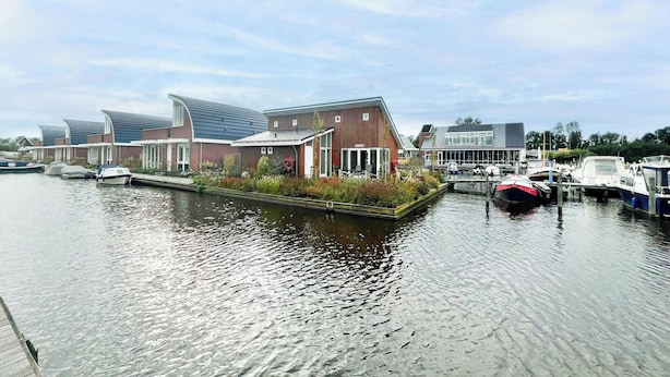 Een gebouw aan een gracht met een aanlegsteiger, boten en een heldere lucht.