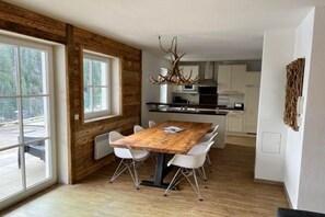 A modern kitchen with a wooden dining table, white chairs, and a unique antler chandelier. - Alpine Apartment Near Ski Lift (Saalbach Hinterglemm)