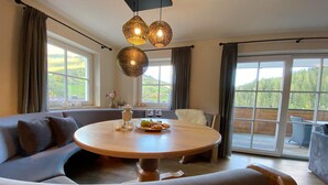 Ein modernes Wohnzimmer mit einem runden Holztisch, grauen Sofas und großen Fenstern mit Blick ins Freie.