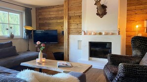 Ein Wohnzimmer mit Kamin, einem aufgehängten Hirschgeweih, einem Fernseher und einem Sofa.