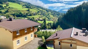Ein zweistöckiges Gebäude mit geneigtem Dach, einer Holzfassade und Blick auf ein grünes Tal mit Häusern und Bäumen.