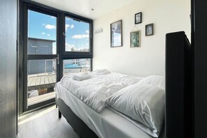 Ein Schlafzimmer mit einem Bett, einem großen Fenster und Blick auf ein Gebäude.