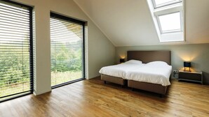 A bedroom with a bed, two bedside tables, a skylight, and large windows. - Villa with Heated Pool, Sauna (Aalten)