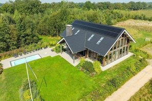 Une maison moderne dotée d’une grande façade vitrée, d’une piscine et d’une pelouse bien entretenue.