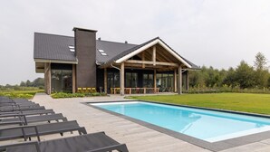 A modern building with a pool, outdoor seating, and a covered patio area. - Villa with Heated Pool, Sauna (Aalten)