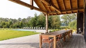 An outdoor deck with a wooden table and chairs, a barbecue grill, and a pool in the background. - Villa with Heated Pool, Sauna (Aalten)
