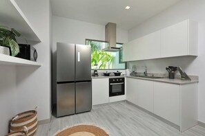 A modern kitchen with white cabinets, stainless steel appliances, and a window with a view of greenery. - Suksan | Naiharn beach | 4-bedroom Pool Villa (Rawai)