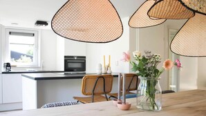 A modern kitchen with a central island, wicker pendant lights, and a vase with flowers on the table. - Modern Coastal Retreat with Garden (Sint Maarten)