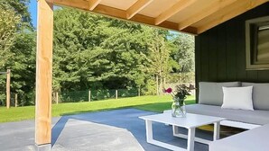 An outdoor seating area with a wooden pergola, a white table with a vase of flowers, and a grey sofa. - Modern Coastal Retreat with Garden (Sint Maarten)