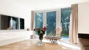 A living room with a flat-screen TV, a round wooden coffee table, a vase with flowers, a wicker chair, and a sofa. - Modern Coastal Retreat with Garden (Sint Maarten)