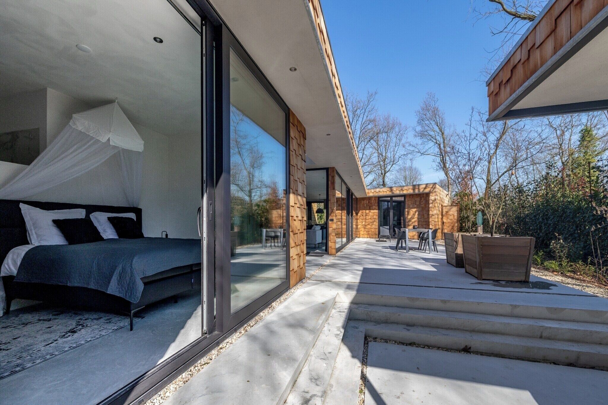 A modern bedroom with a large bed, a glass door leading to a patio, and a stone wall.