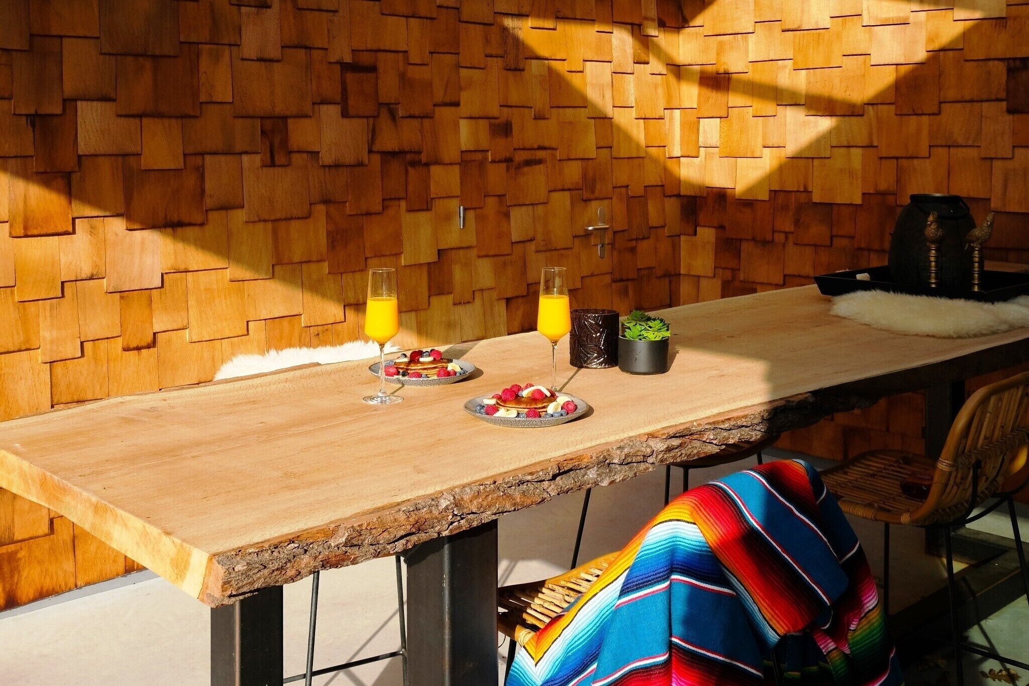 Un tavolo da pranzo in legno con piatti di cibo e bevande, una sedia e un muro con un motivo geometrico.