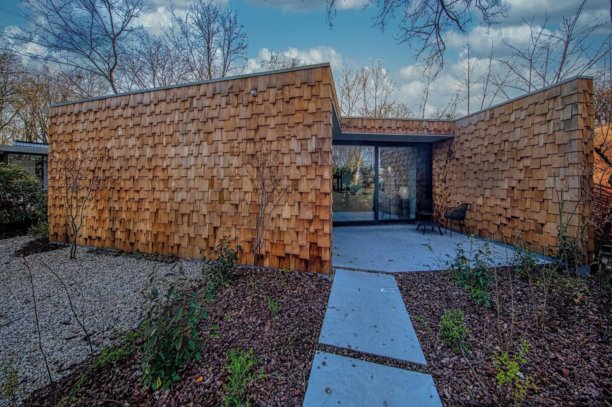 Un bâtiment moderne doté d’une façade en bois, d’une entrée en verre et d’un chemin menant à un espace aménagé avec des sièges.