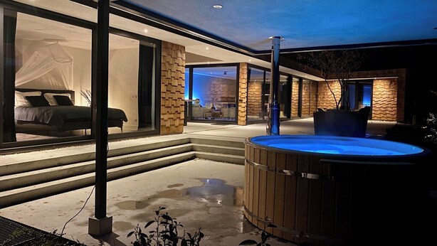 A modern outdoor living area with a hot tub, a covered seating area, and a view into the interior. - Wellness Villa with Private Hot Tub (Oosterhout)