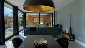 A modern interior with a dining table, black chairs, a large black pendant light, and a view through large windows. - Wellness Villa with Private Hot Tub (Oosterhout)