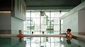 A modern indoor swimming pool with clear glass walls, a minimalist design, and a view of greenery outside. - Wellness Villa with Private Hot Tub (Oosterhout)