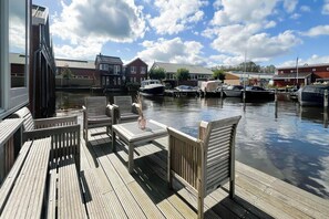 Eine Holzterrasse mit Sitzgelegenheiten und Blick auf einen Yachthafen mit Booten.