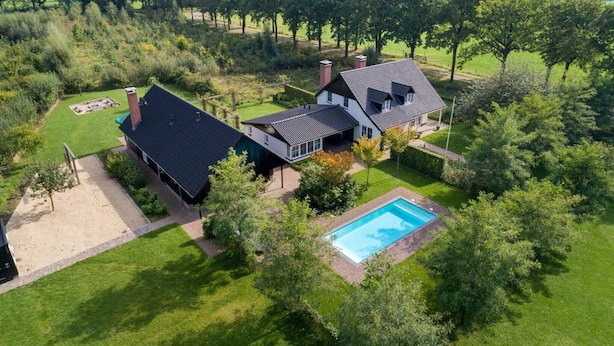 Una casa con piscina, rodeada de césped cuidado y árboles.