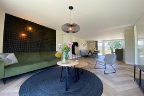 A modern living room with a green sofa, a round coffee table with a vase, a hanging light fixture, and a dining area in the background. - Coastal Home with Garden for 6 (Sint Maarten)