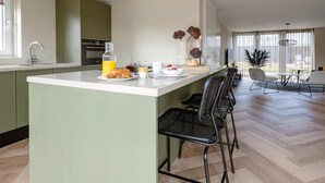 Una cocina moderna con una isla central, un comedor con mesa y sillas, y vistas al exterior.