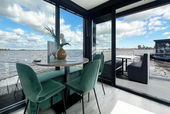 Un interior moderno con una mesa redonda y sillas, un florero, y vista al agua.